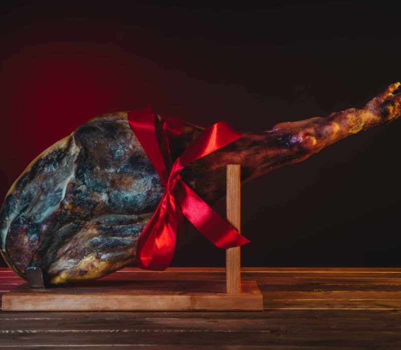 spanish ham placed in ham holder on a wooden table isolated with red and black background with a red gift bow of christmas